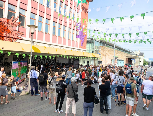 Eine Menschengruppe steht vor dem ruru Haus und hört zu der Band zu.
