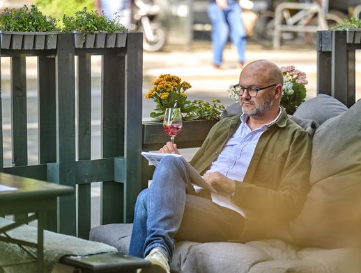 Ein Mann sitzt gemütlich im Außenbereich des Holy Nosh und liest eine Zeitschrift. 