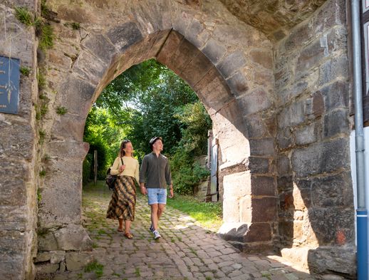 Zwei Personen sparzieren durch den Torbogen in der Stadtmauer von Grebenstein